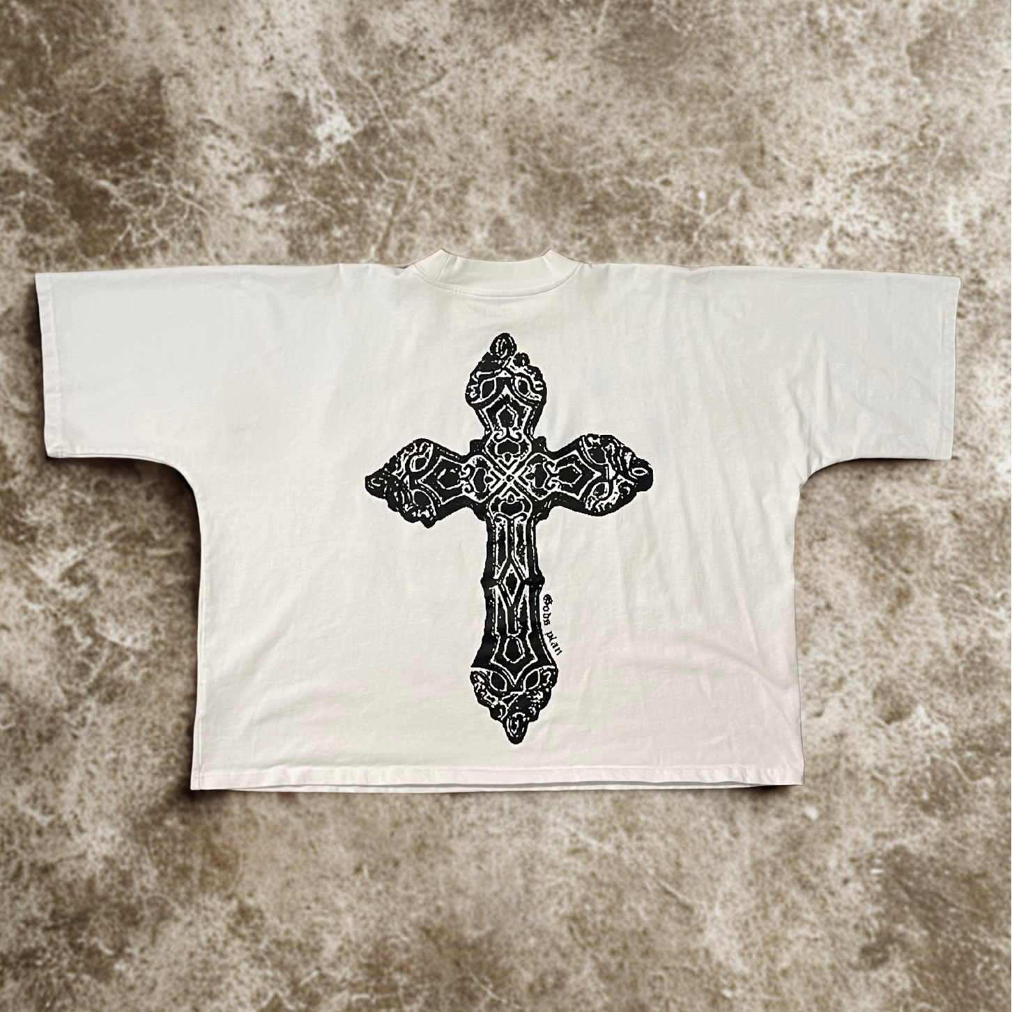 White t-shirt with a black cross design on a textured brown background